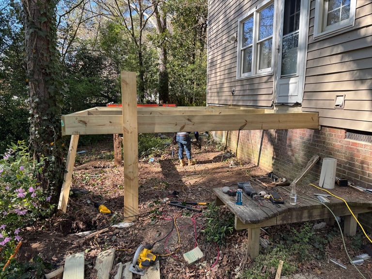 Wooden pergola frame under construction in a backyard beside a house with construction materials and tools scattered around