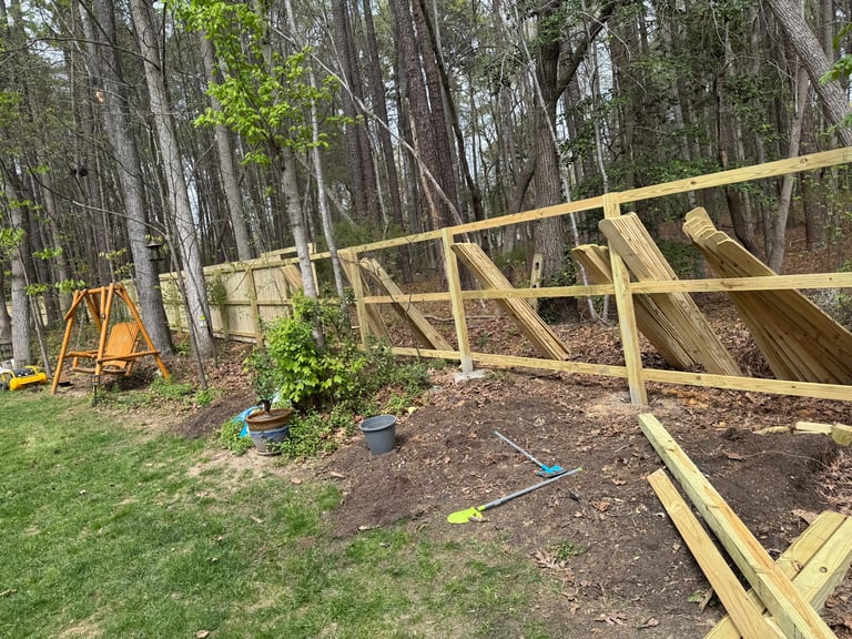 Wooden deck frame under construction in a wooded backyard with trees, yellow swing set, and grass