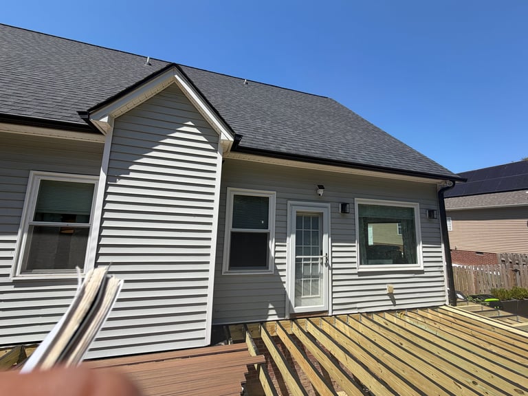 Modern single-story house with white and gray siding, peaked roof, and composite deck under clear blue sky