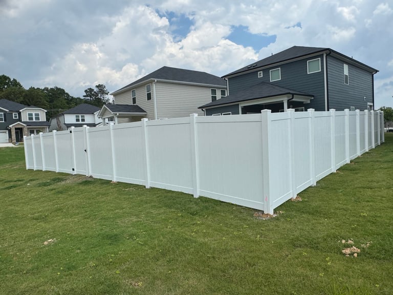 White vinyl privacy fence surrounding residential backyard with two-story gray house and cloudy sky
